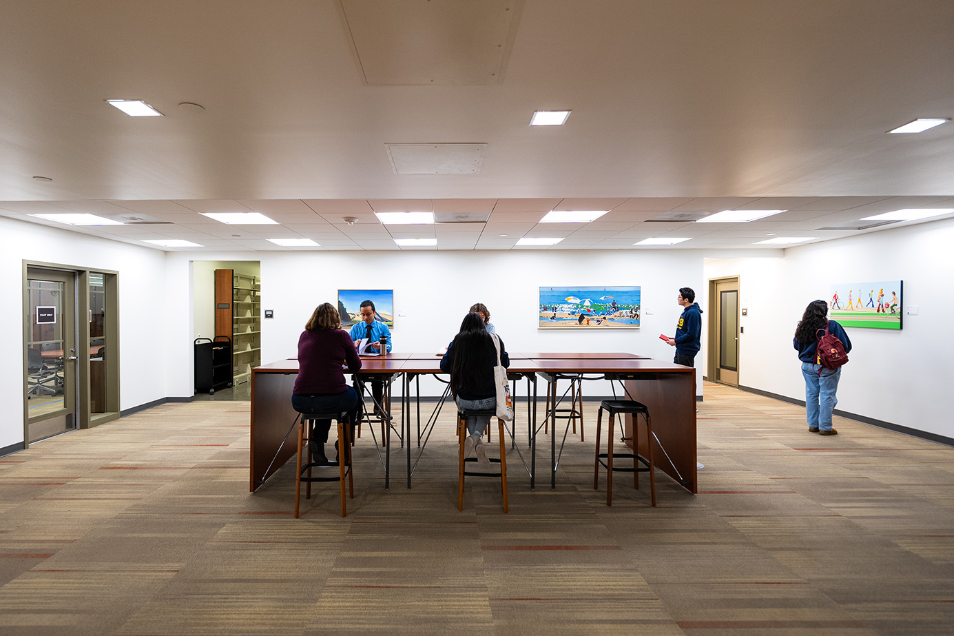 People at a table and viewing artwork in the Sara Miller McCune Arts Library