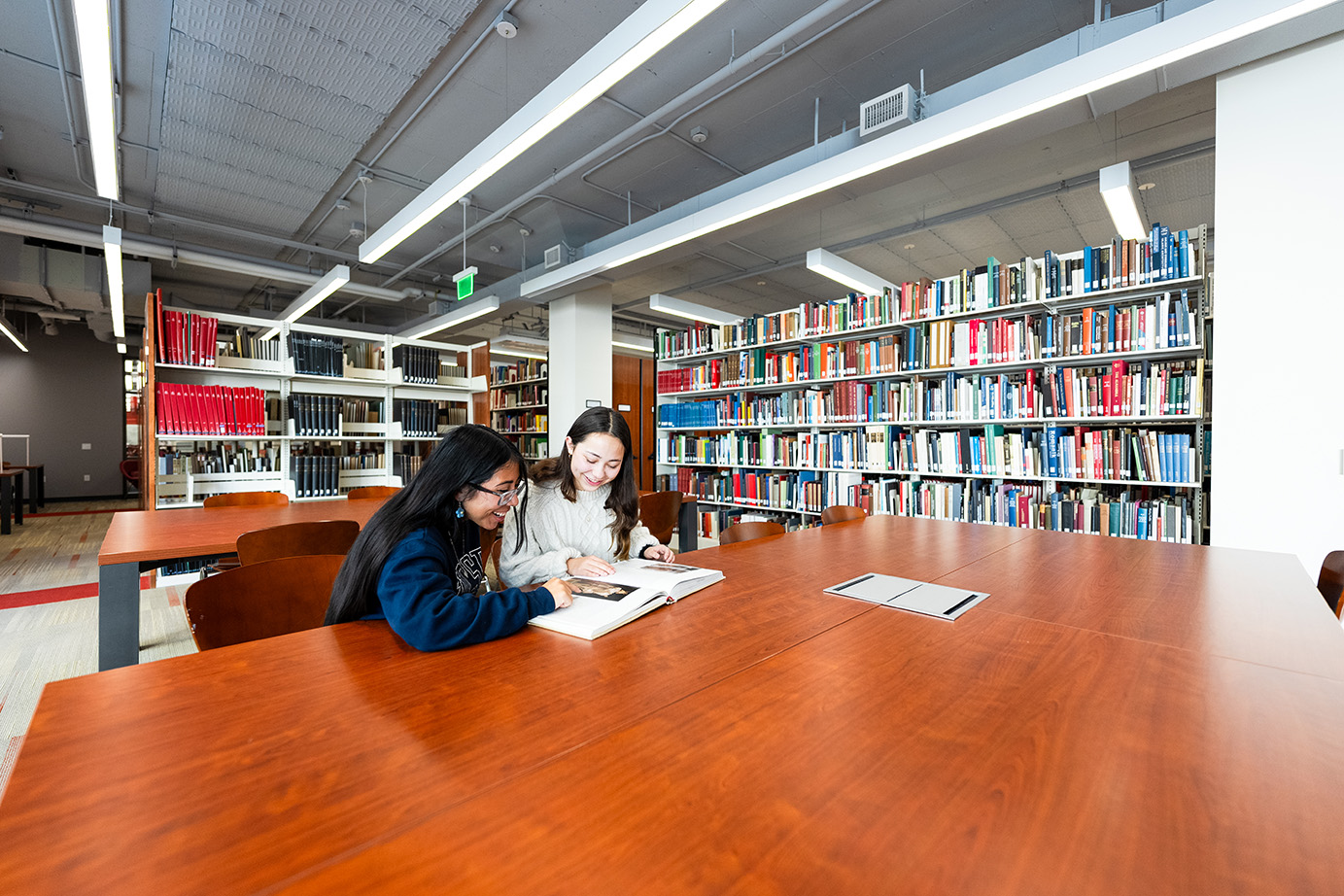 Two people reading a book at table in the Sara Miller McCune Arts Library